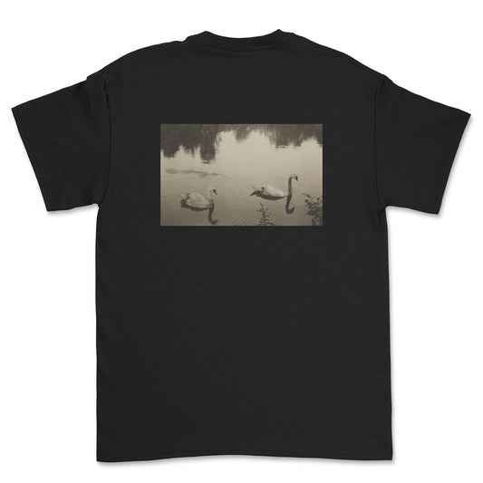 Black t-shirt with a printed design of ducks on a lake on the back, on a white background.